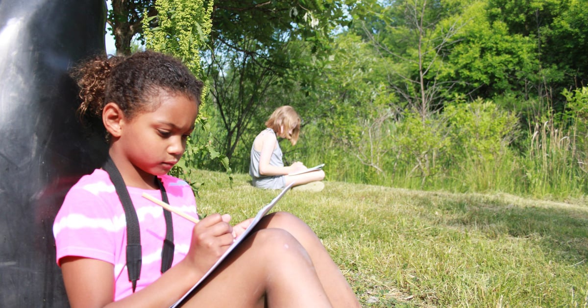 Two girls sitting down on the grass writing